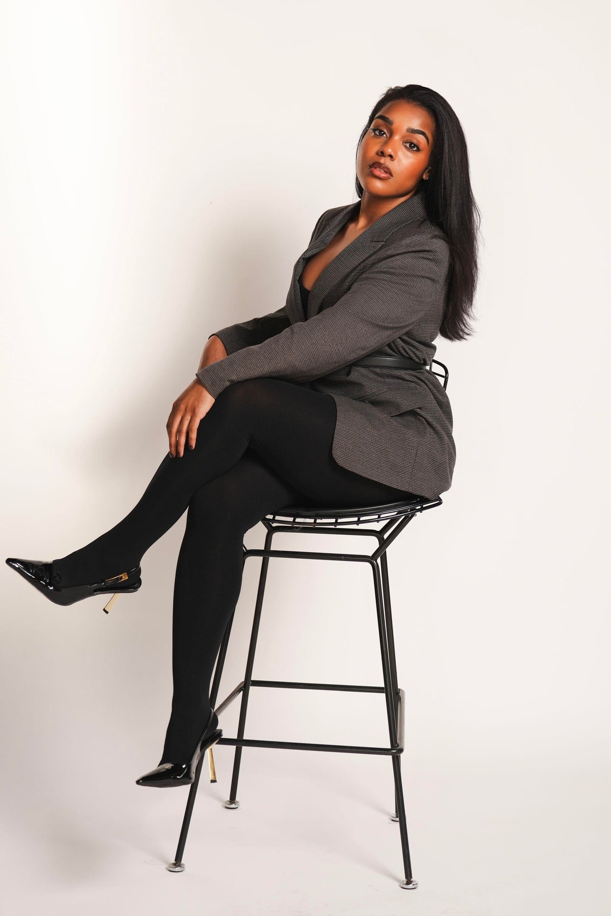 Founder sitting on a black stool wearing a gray blazer and black pants against a white background